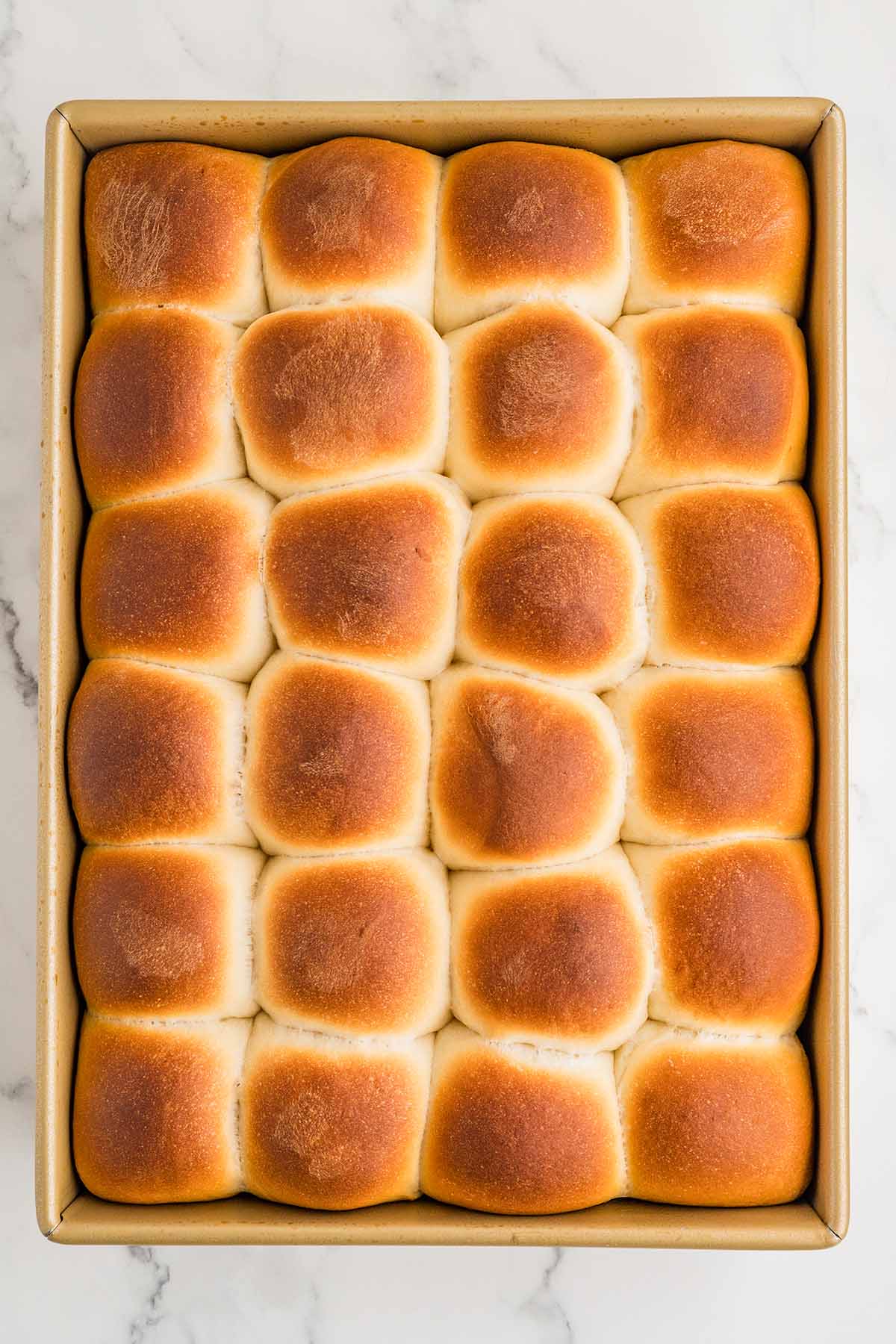 Freshly baked cafeteria rolls with golden brown tops in a gold baking pan.