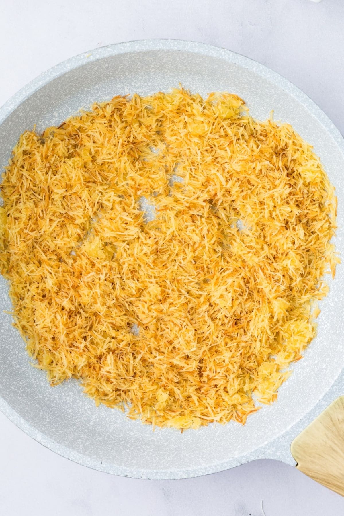 Golden toasted kataifi pastry in a nonstick skillet with a wooden spatula.