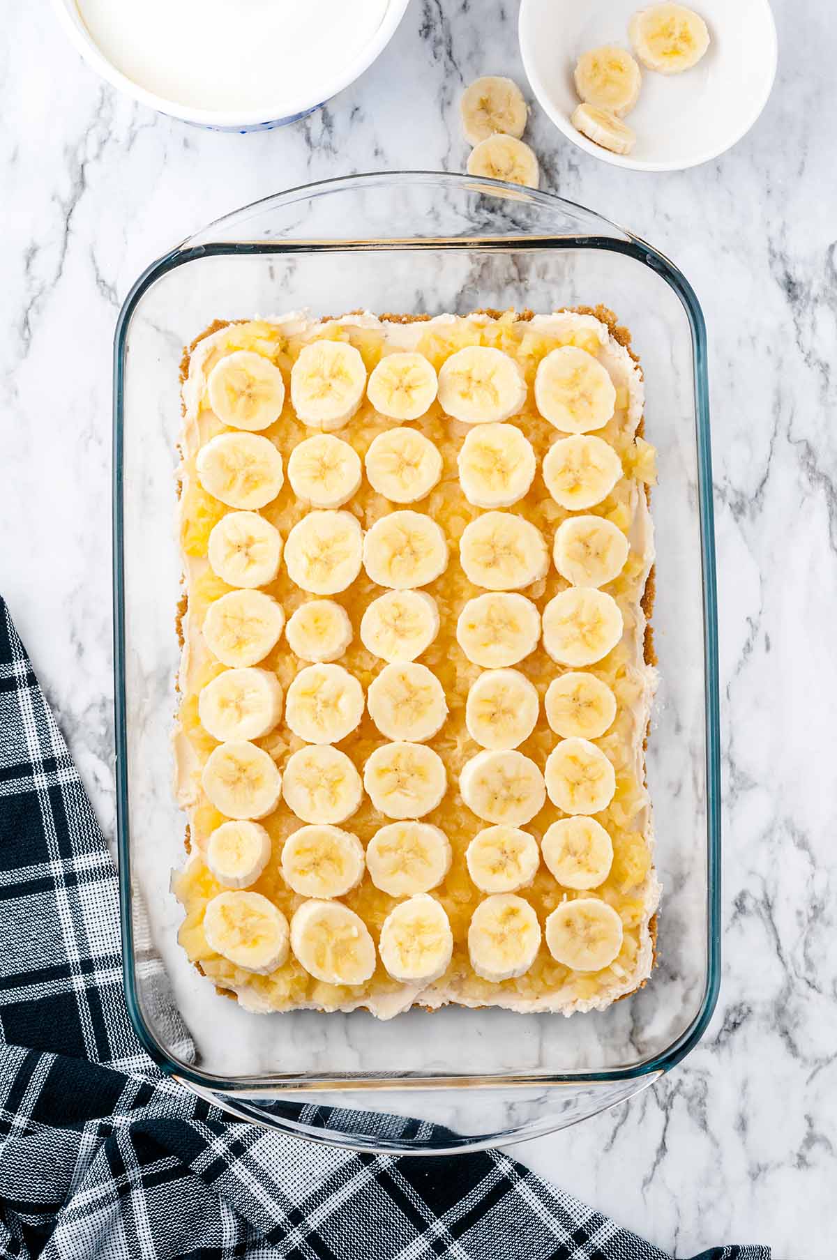 Sliced bananas arranged in rows over the pineapple layer in the glass baking dish.