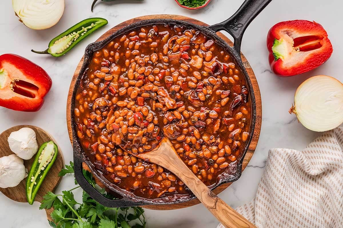 Smoked baked beans in a cast iron skillet with a wooden spoon.
