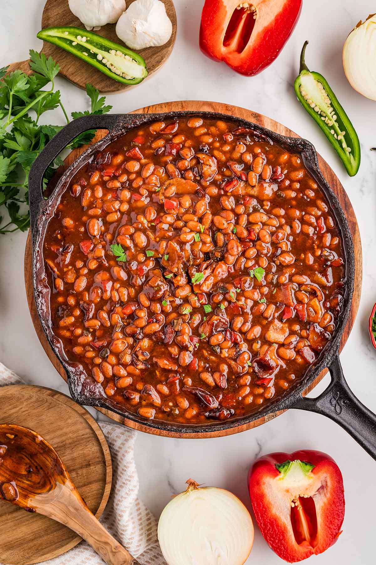 Smoked baked beans in a cast iron skillet with a wooden spoon onside.