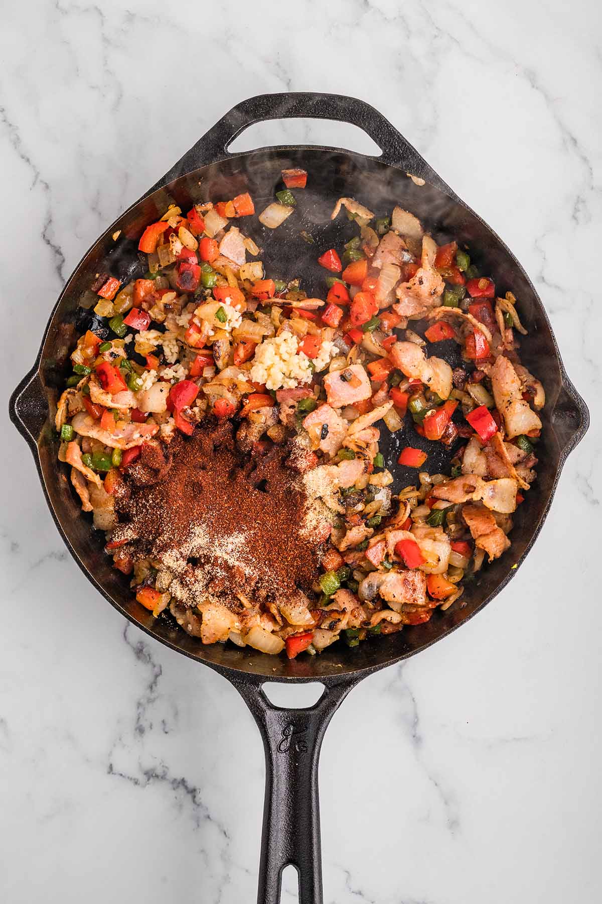 Saut&eacute;ed bacon, peppers, onions, garlic, and spices in a cast iron skillet for smoked baked beans.