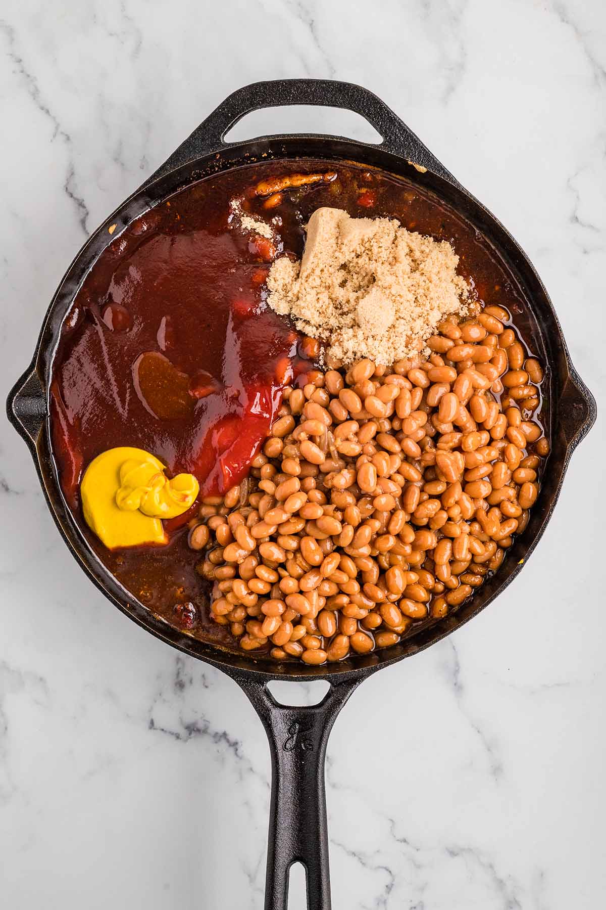 Pinto beans, BBQ sauce, brown sugar, ketchup, and mustard added to the cast iron skillet.