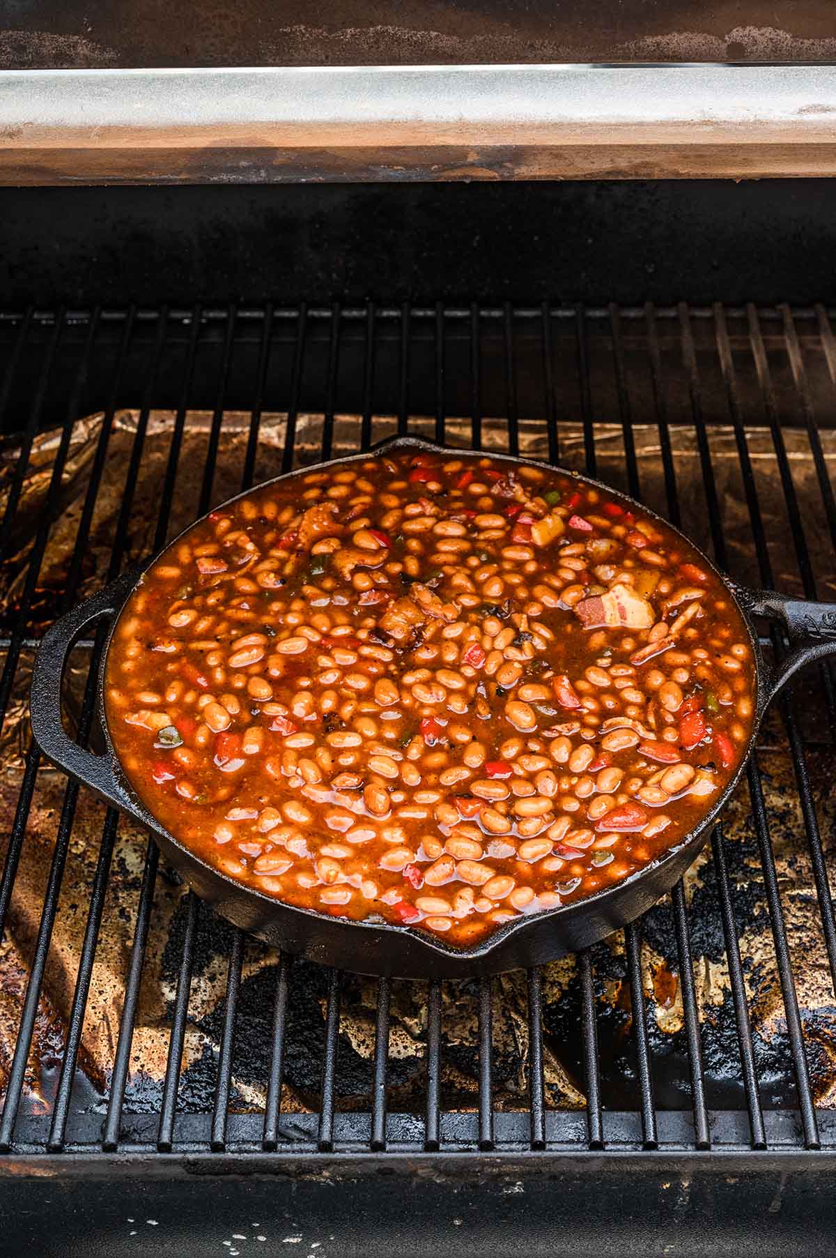 Cast iron skillet of baked beans placed on the grill grates of a pellet smoker.