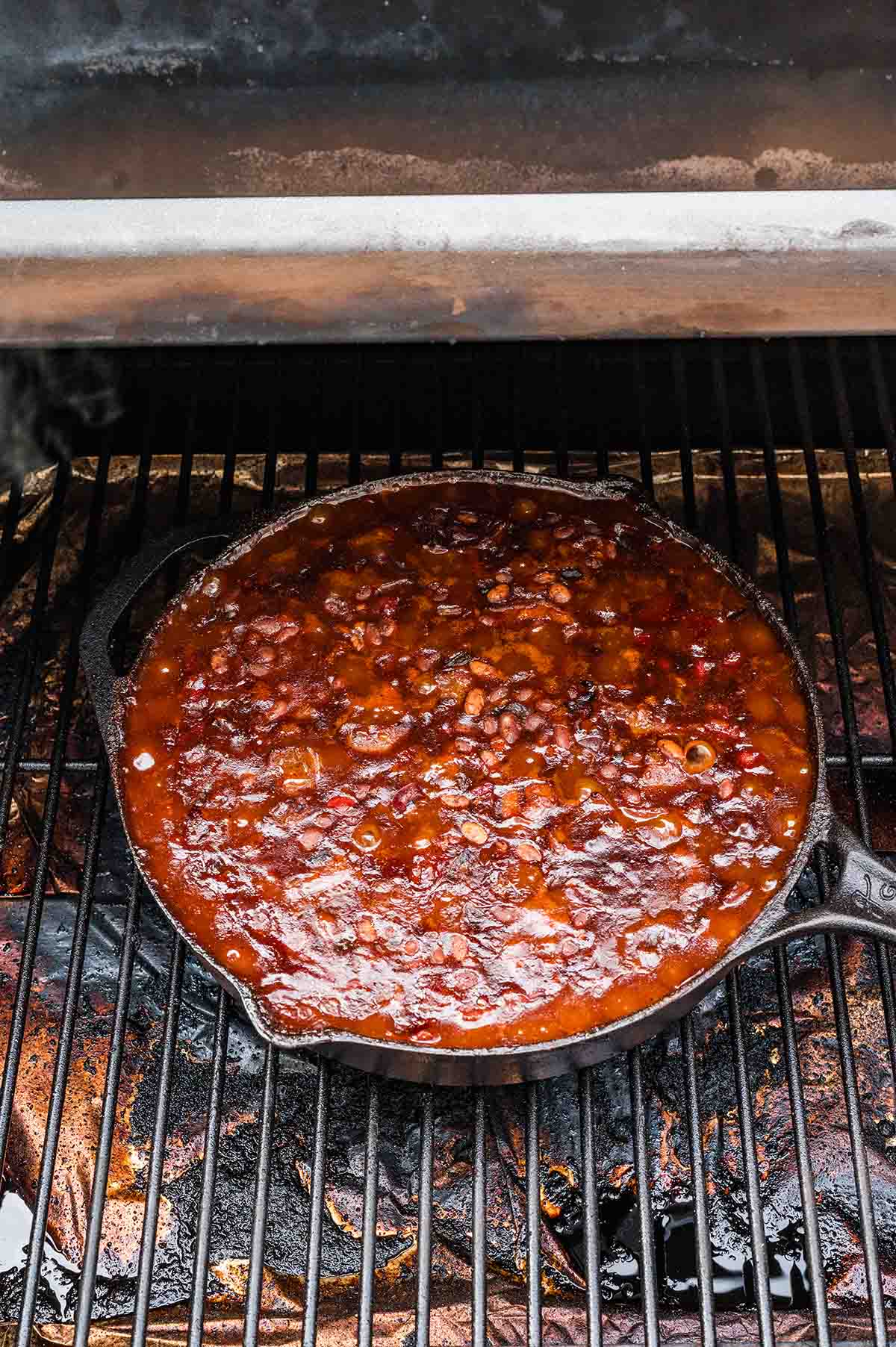 Smoked baked beans bubbling and caramelizing in a cast iron skillet on the smoker.