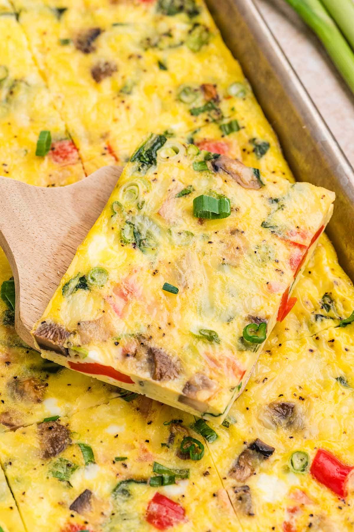 Slice of veggie egg bake with peppers, mushrooms, and green onions lifted on a spatula.