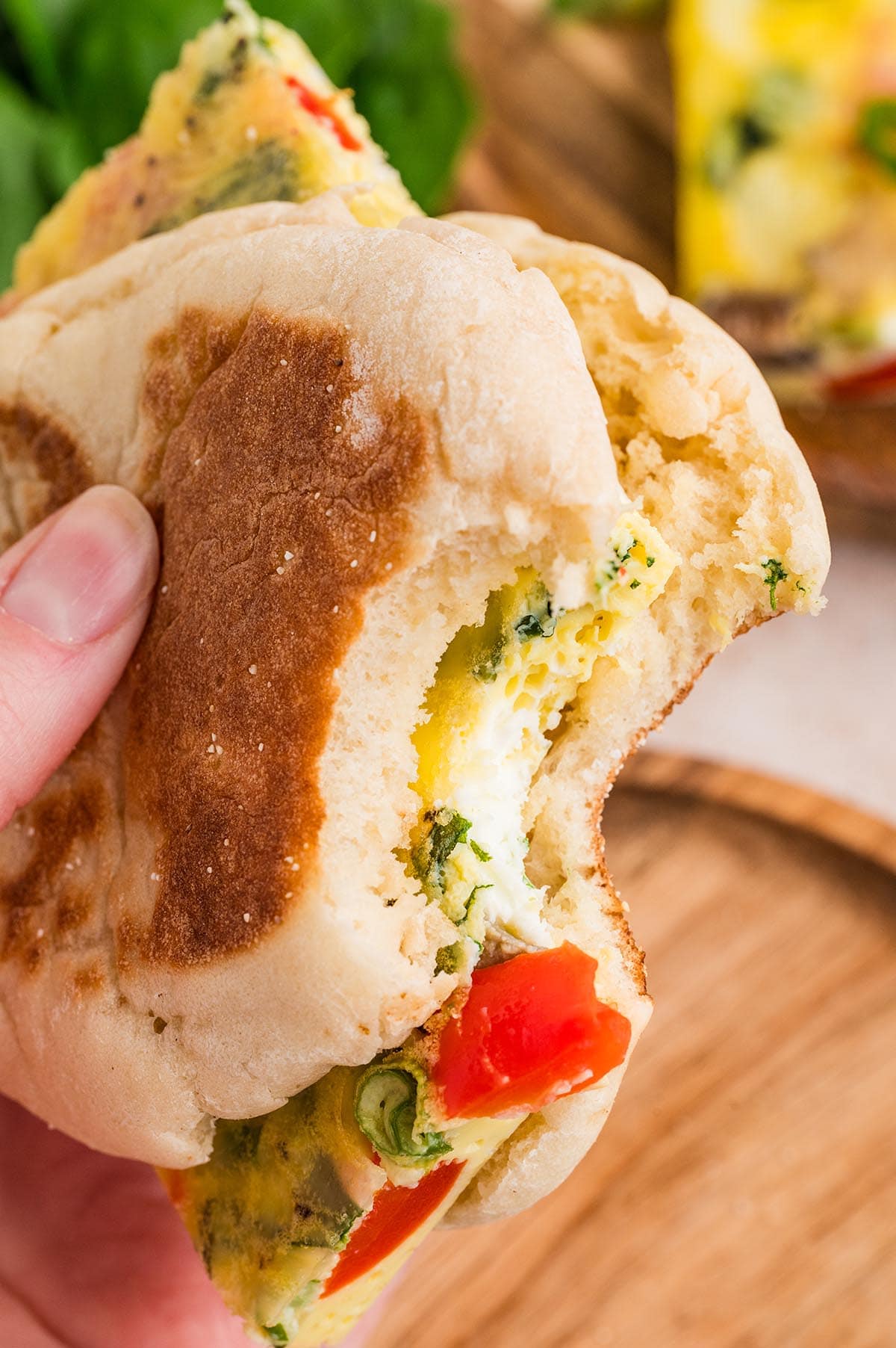Breakfast sandwich with veggie egg bake, peppers, and greens inside an English muffin.