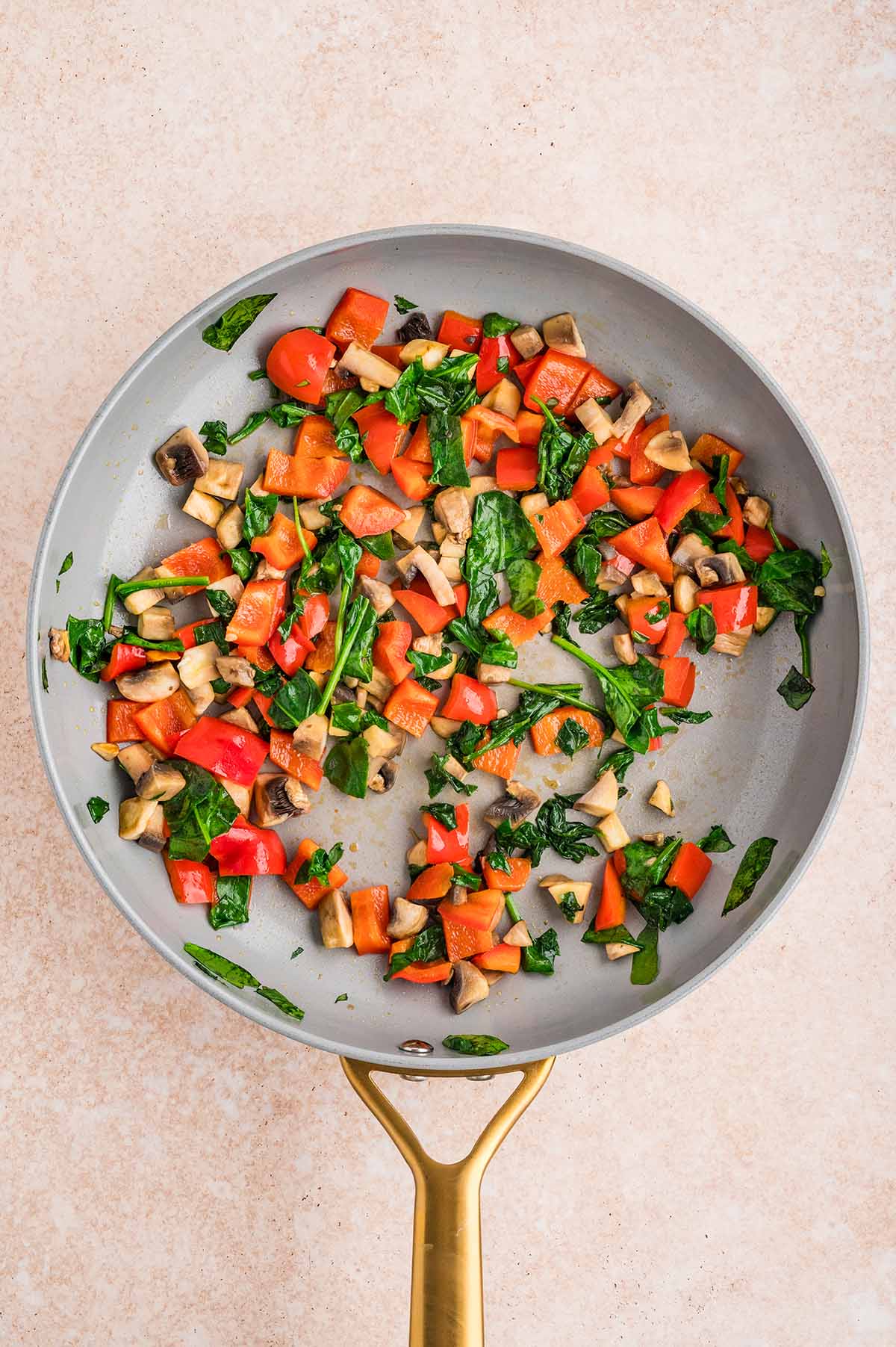 Sautéed mushrooms, bell peppers, and spinach cooking in a skillet.