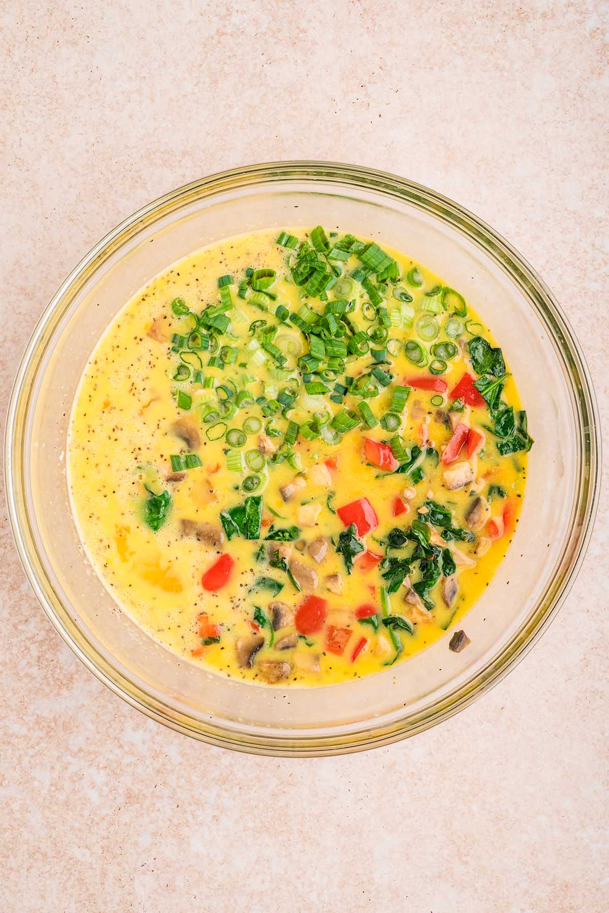 Egg mixture with sautéed vegetables and green onions in a bowl.
