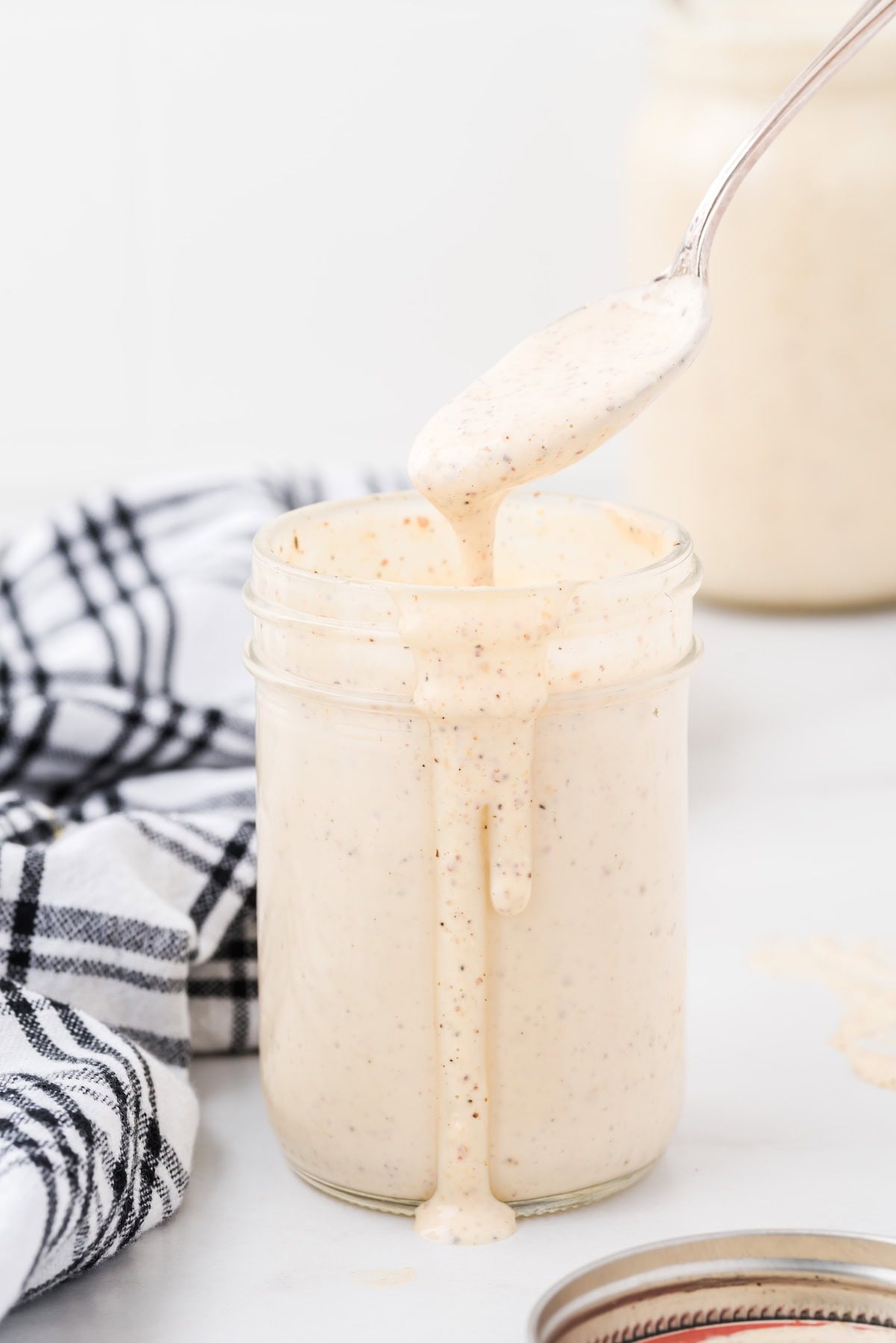 A spoon drizzling Alabama white sauce into a mason jar, with the sauce dripping down the side.