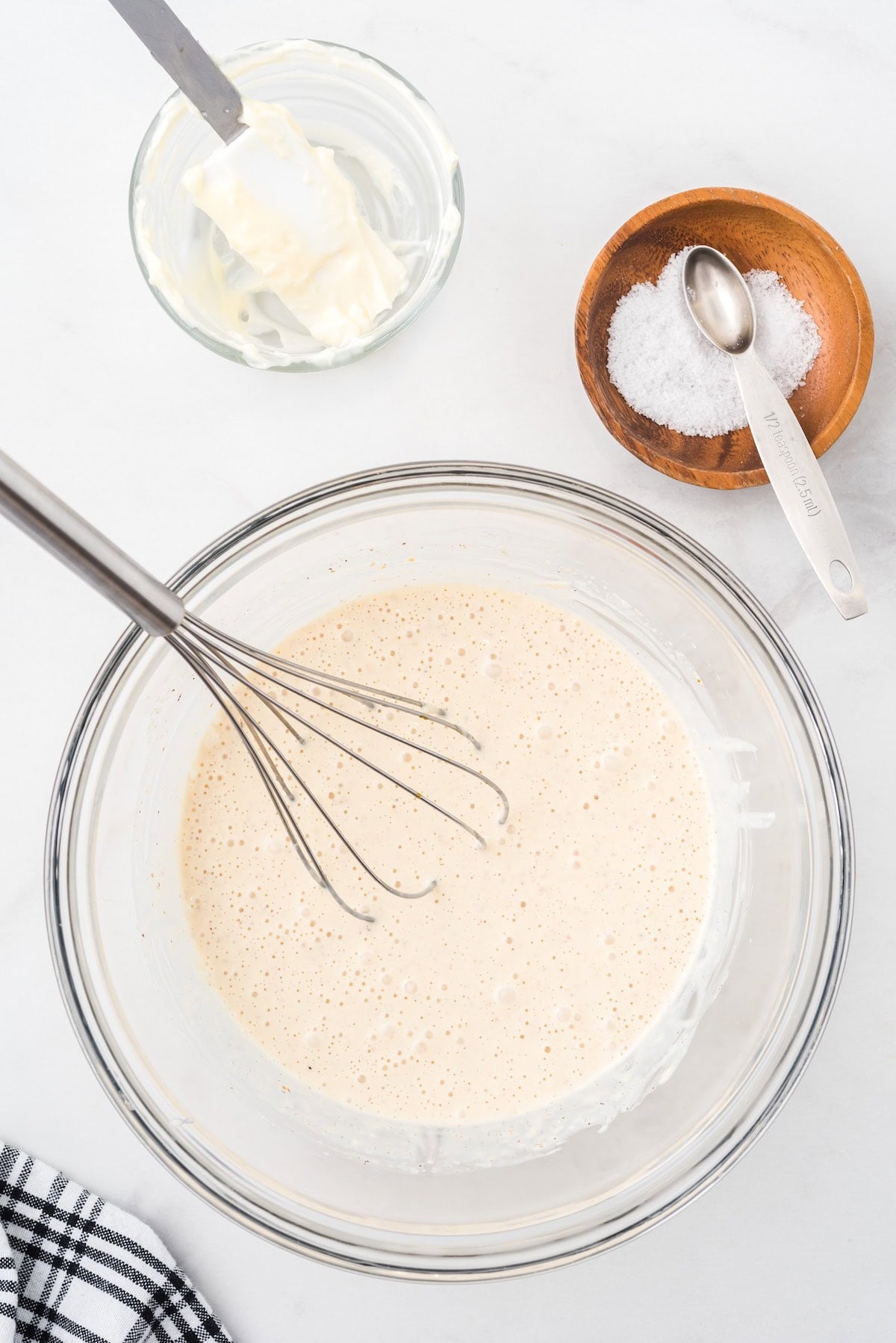 Alabama white sauce being whisked together in a glass bowl, with mayonnaise and salt nearby.
