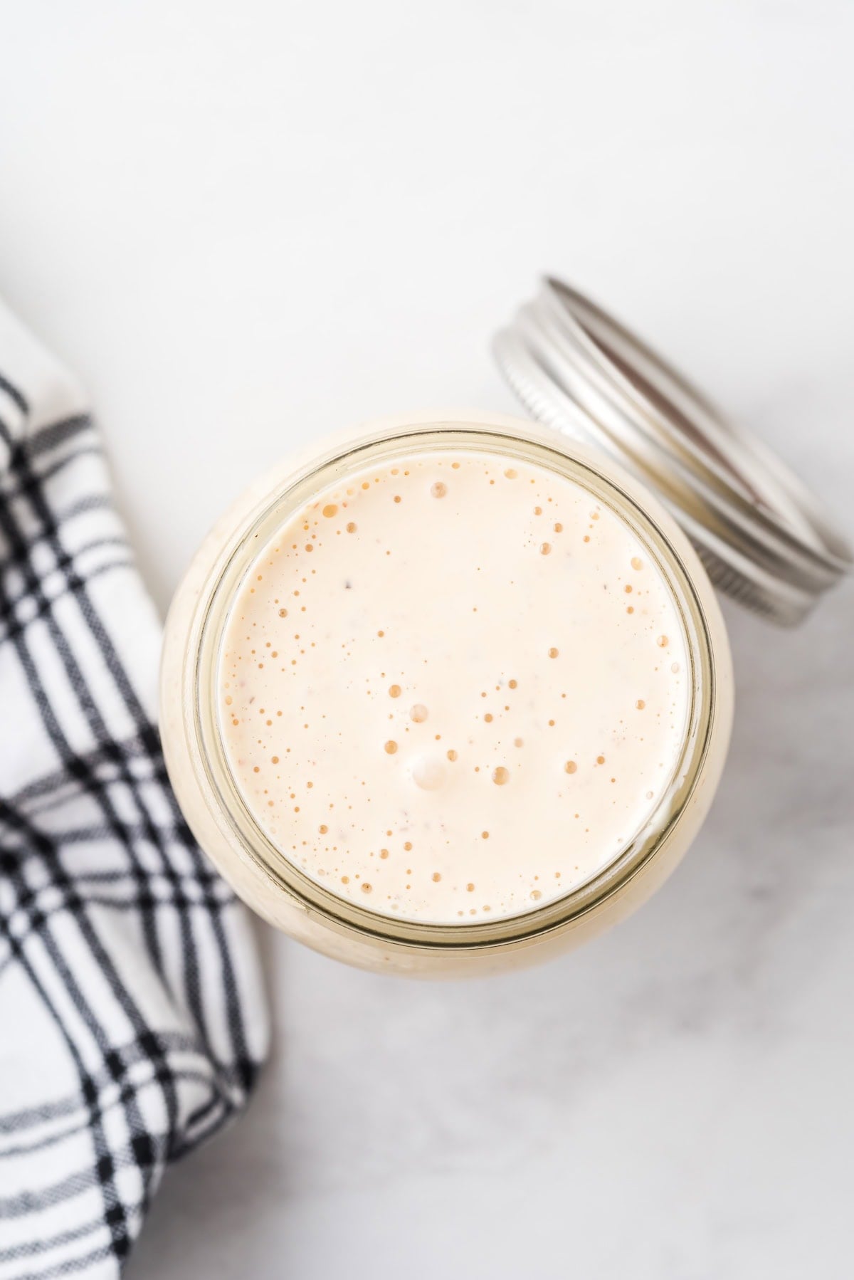 Overhead view of Alabama white sauce in an open mason jar with the lid beside it.