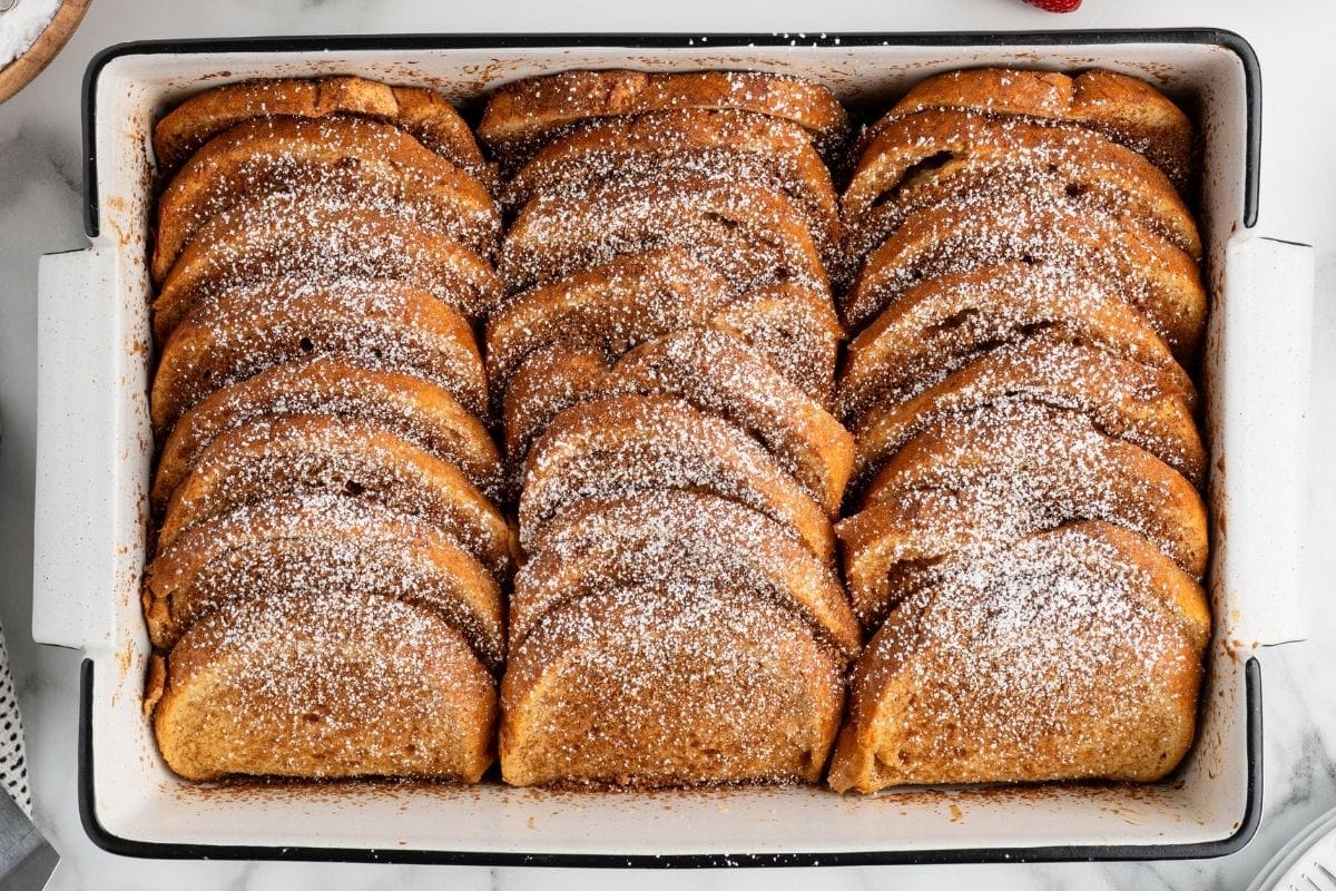 Baked French toast dusted with powdered sugar in a white baking dish.