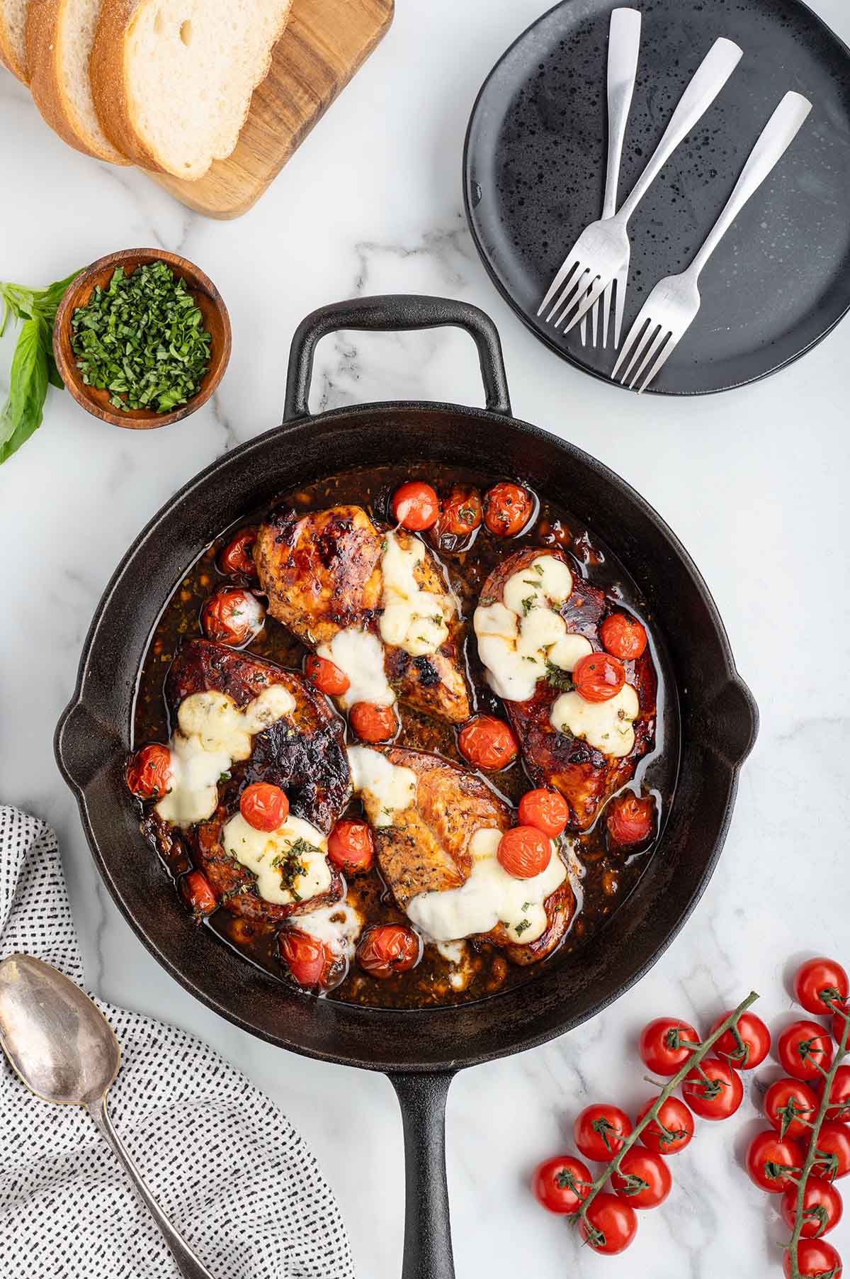 Finished balsamic chicken in skillet fresh from the oven, tomatoes burst, cheese melted, fresh basil on top