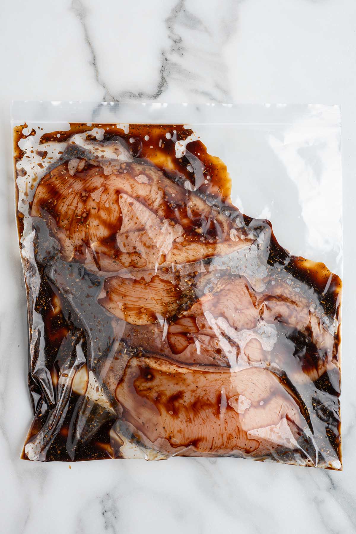 Chicken sealed in zip top bag with marinade, resting on counter.