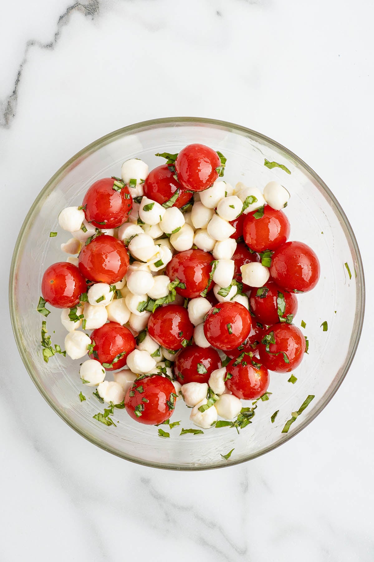 Cherry tomatoes, mozzarella pearls, and fresh basil mixed together in a small bowl.