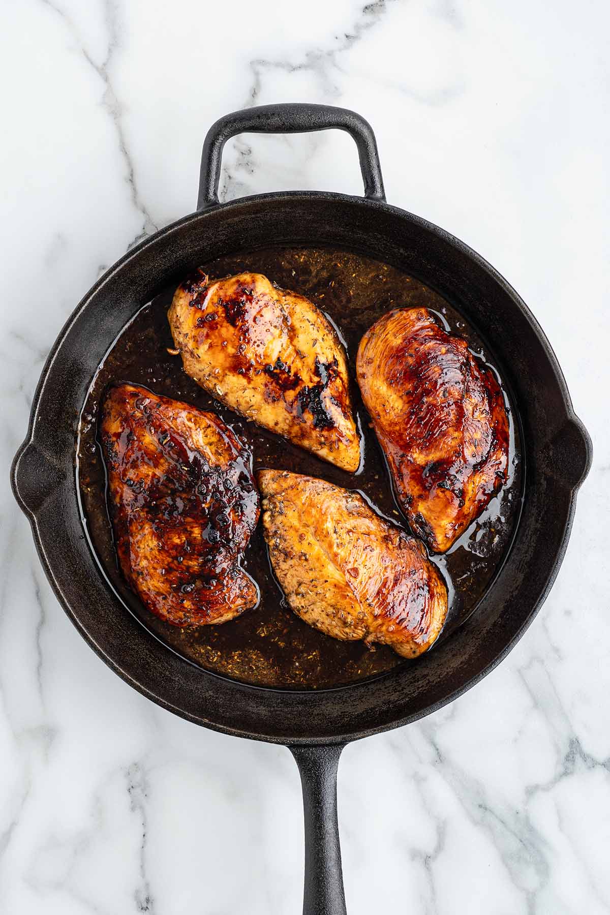 Marinade being poured around the chicken in the skillet.
