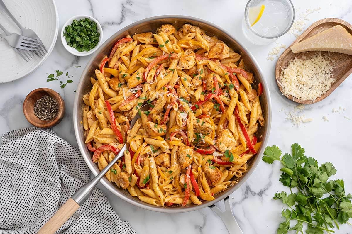 Cajun chicken pasta with bell peppers in a large skillet garnished with parmesan and fresh parsley.