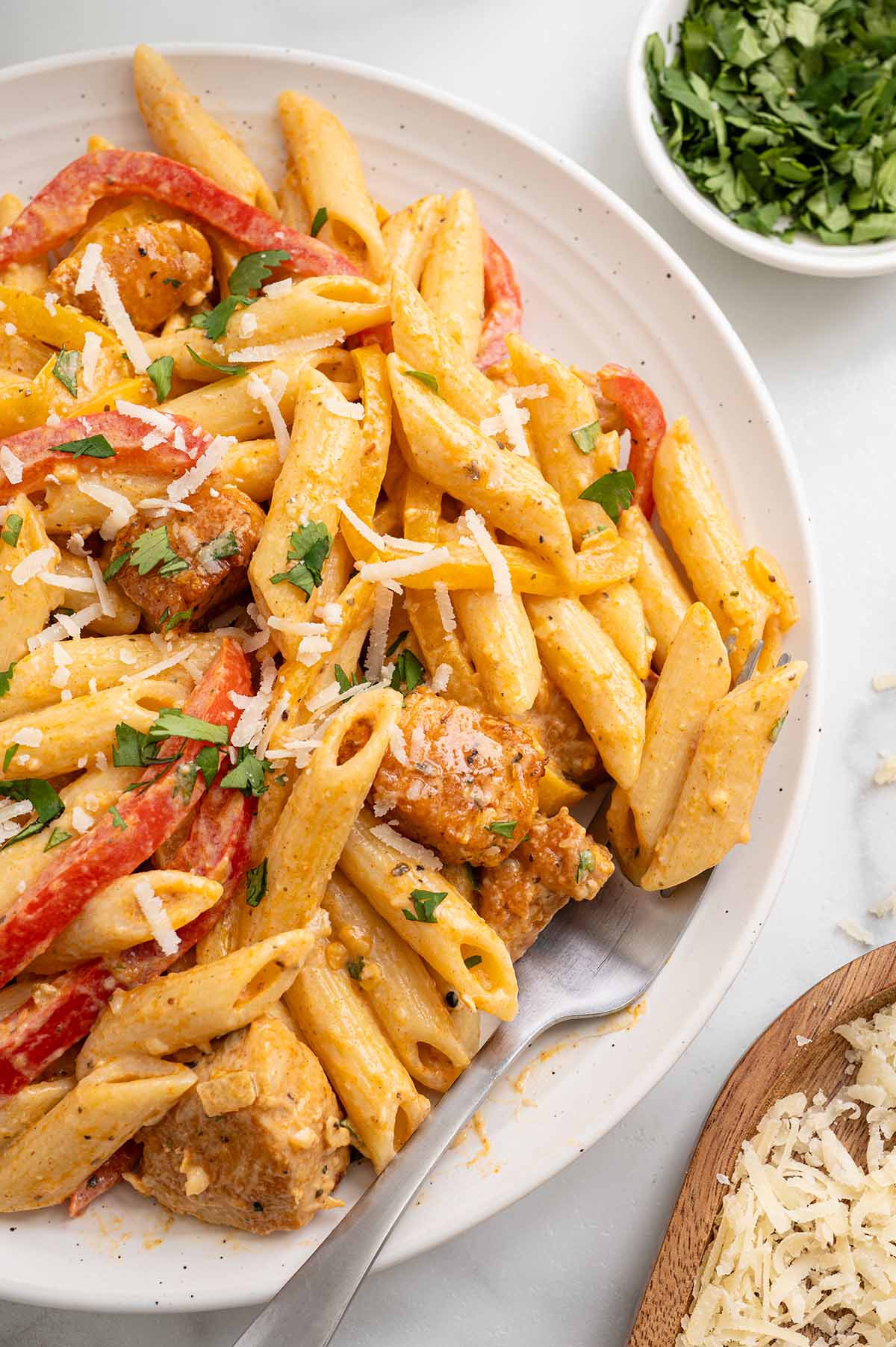 Close-up of Cajun chicken pasta with bell peppers on a white plate topped with shredded parmesan and fresh parsley.