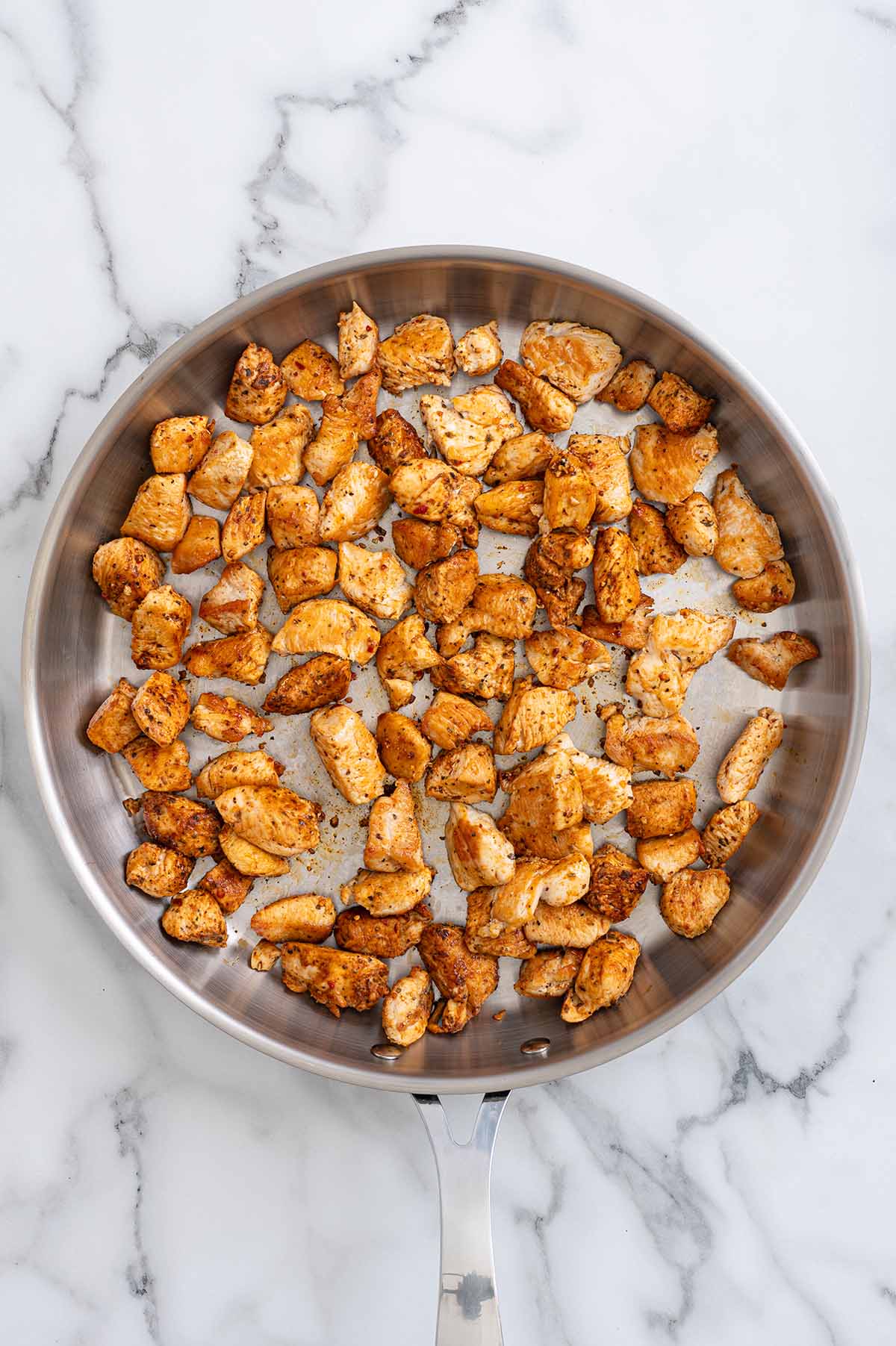 Cajun seasoned chicken pieces cooked in a stainless steel skillet.