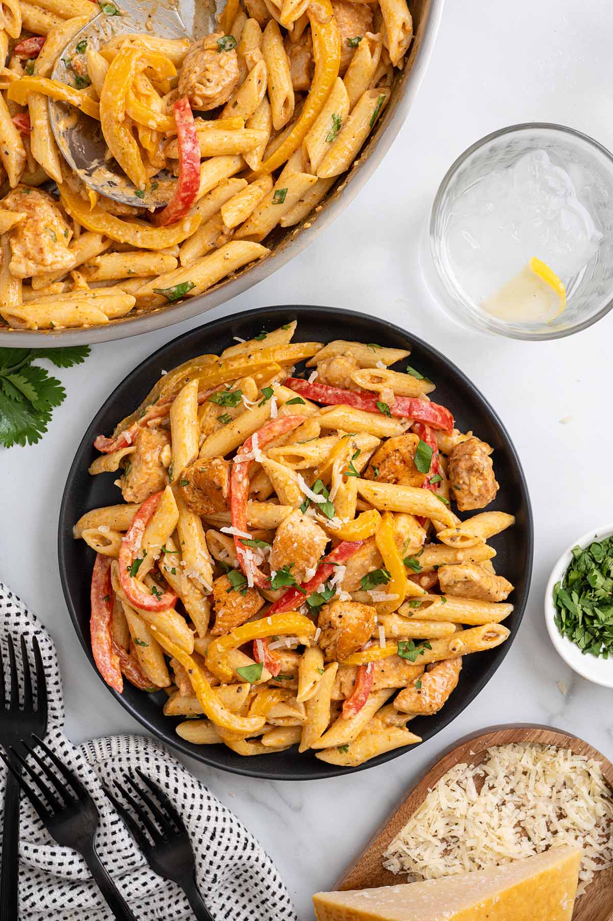 Cajun chicken pasta with bell peppers served in a black bowl with parmesan and fresh parsley alongside the skillet.