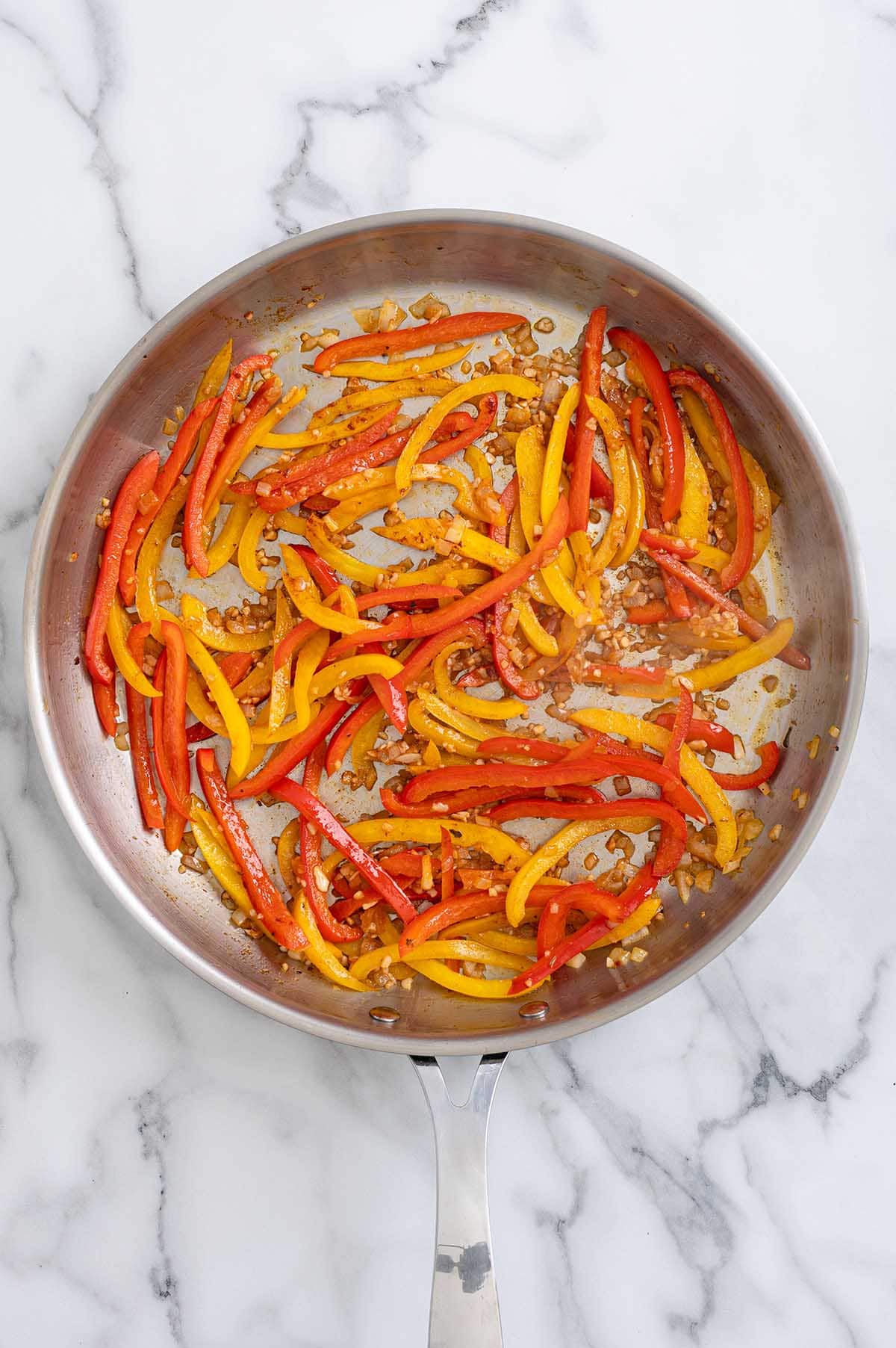 Sautéed red and yellow bell pepper strips with garlic in a stainless steel skillet.