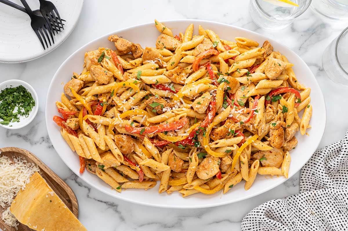 Cajun chicken pasta with bell peppers on a large white oval serving platter garnished with parmesan and parsley.