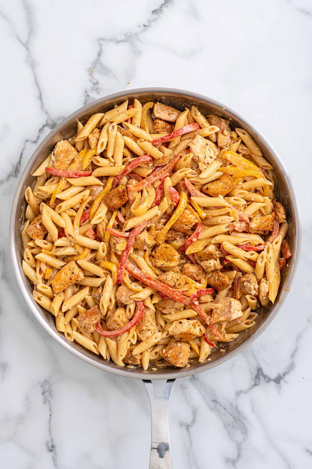 Fully combined Cajun chicken pasta with bell peppers tossed together in a skillet.