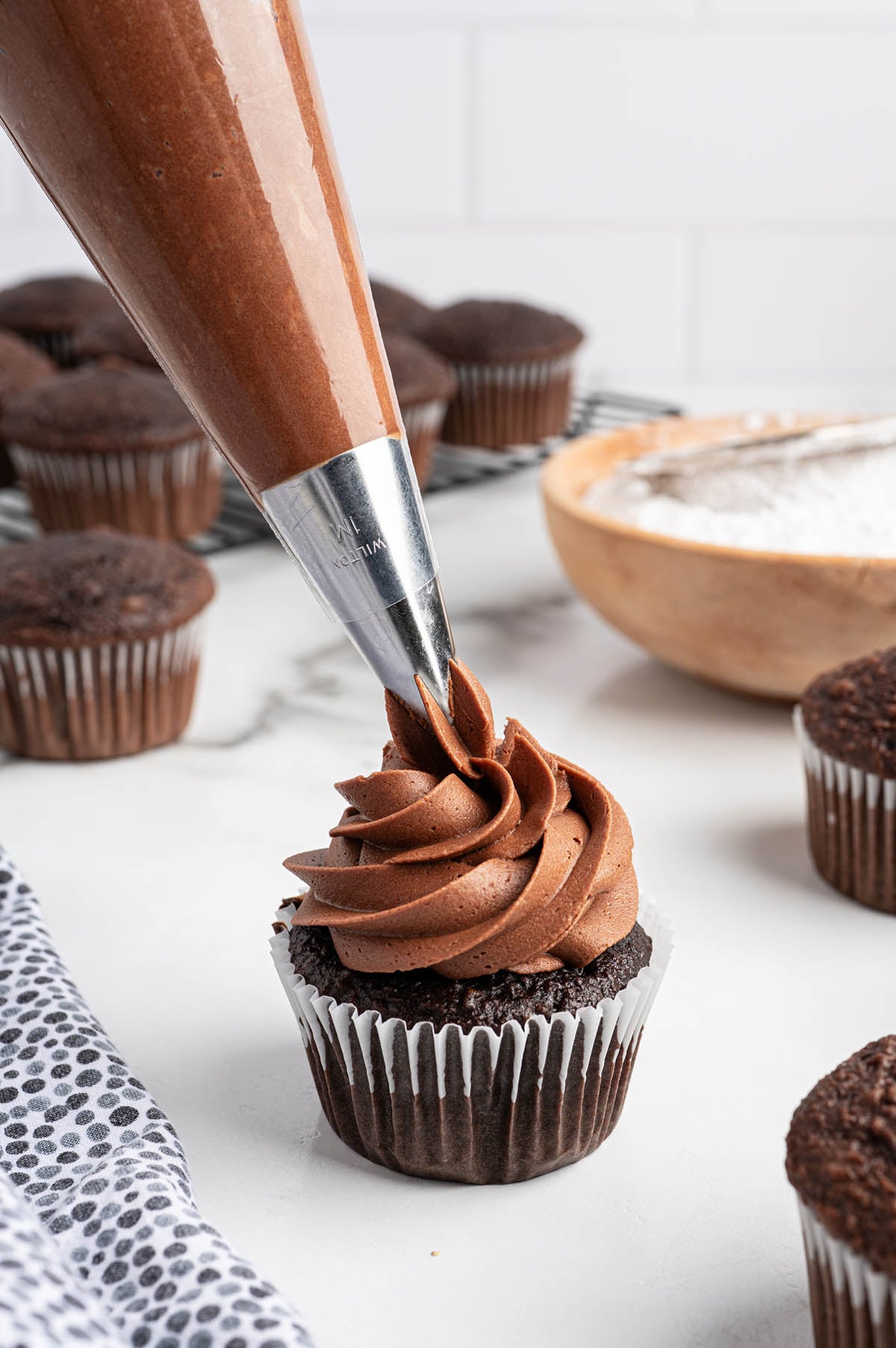 Piping chocolate buttercream frosting onto a chocolate cupcake with a Wilton tip.