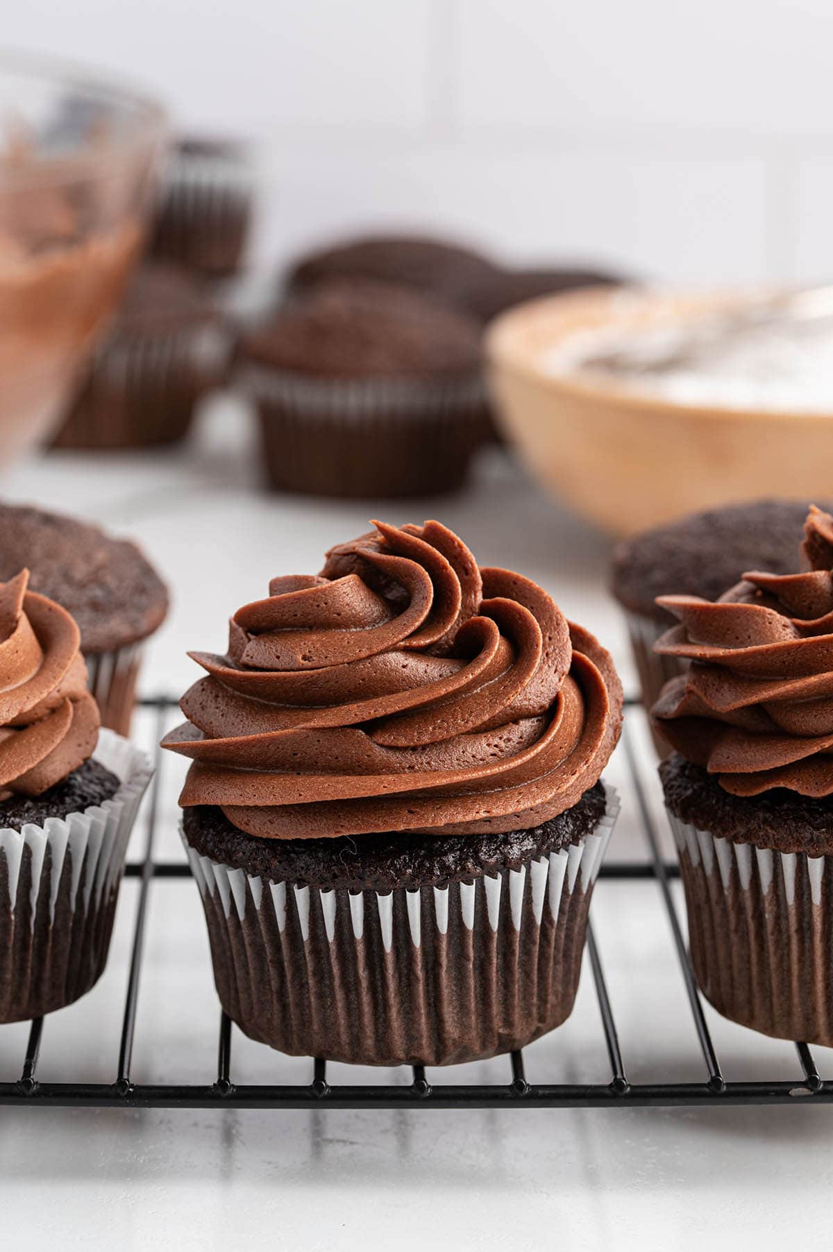 Chocolate cupcakes with swirled chocolate buttercream frosting on a wire cooling rack.