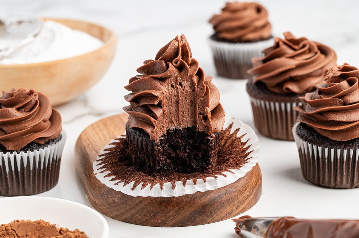 Chocolate cupcake with a large swirl of chocolate buttercream frosting with a bite taken out on a wooden board.