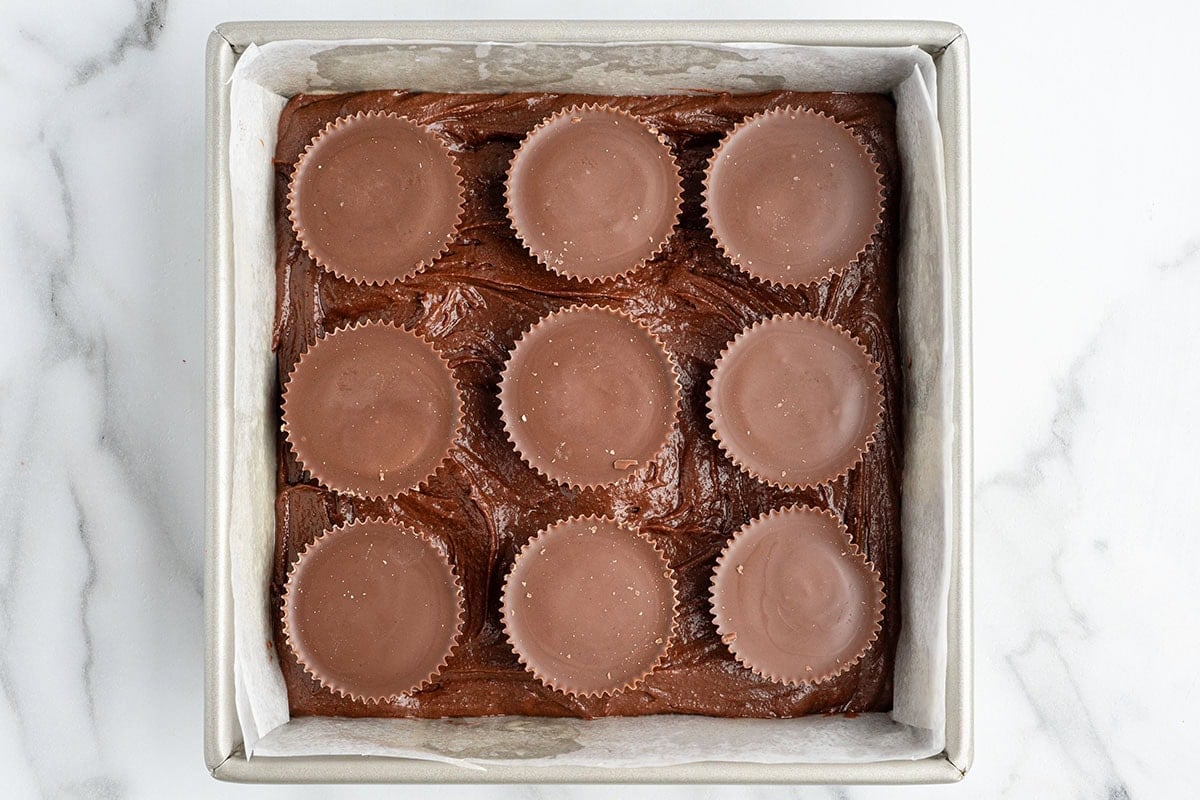 Square pan of fudgy chocolate brownies topped with nine peanut butter cups on marble.