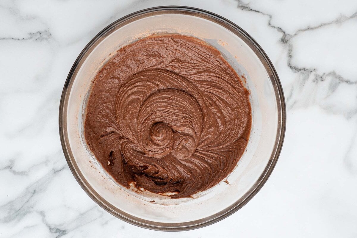 Bowl of thick chocolate brownie batter in a glass mixing bowl on marble counter.