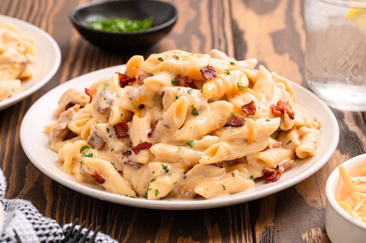 A heaping plate of crack chicken penne with crispy bacon and parsley on a white plate.