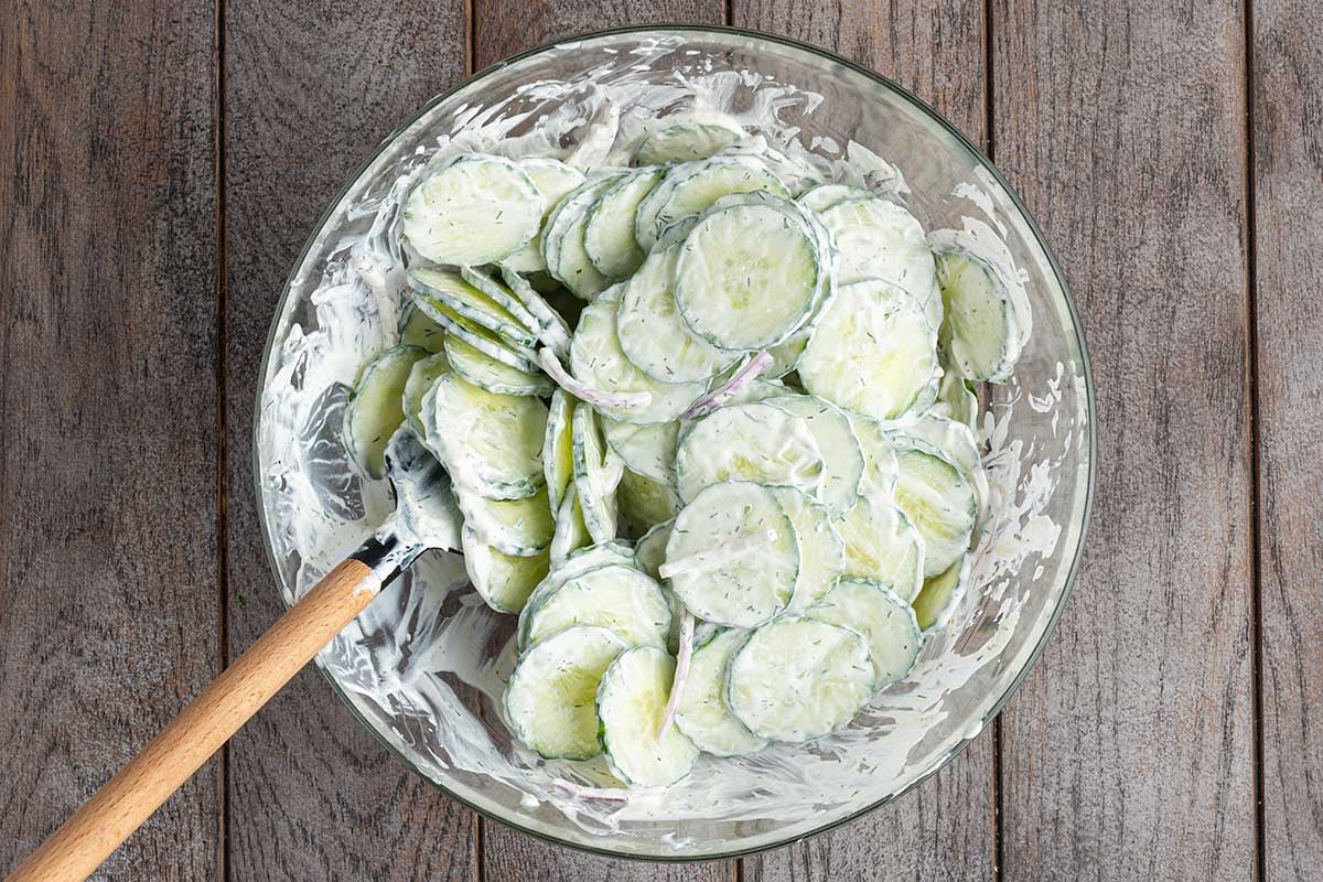 Creamy cucumber salad in a glass bowl with a mixing spoon.