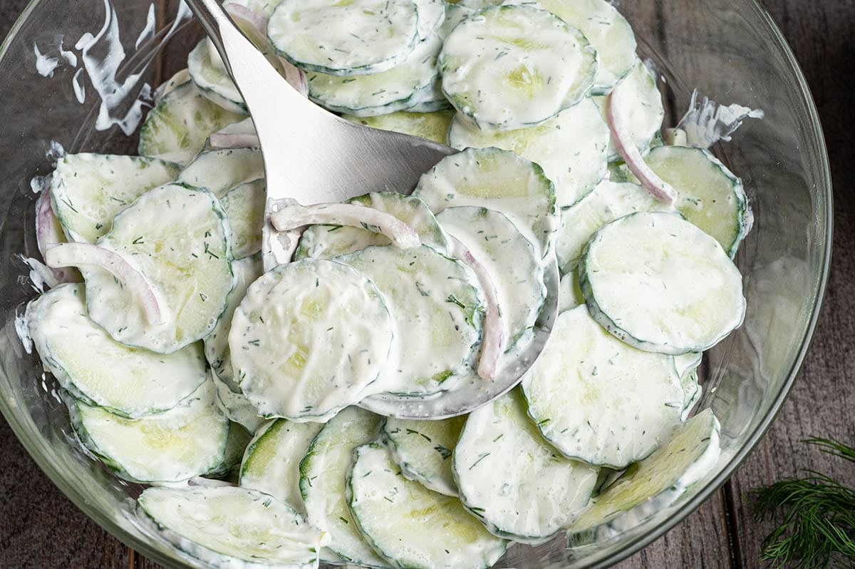 Close-up of creamy cucumber salad with sliced onions and a serving spoon.