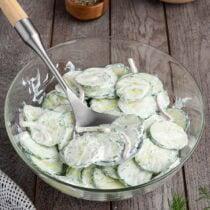Creamy cucumber salad with sliced cucumbers and onions in a glass bowl.