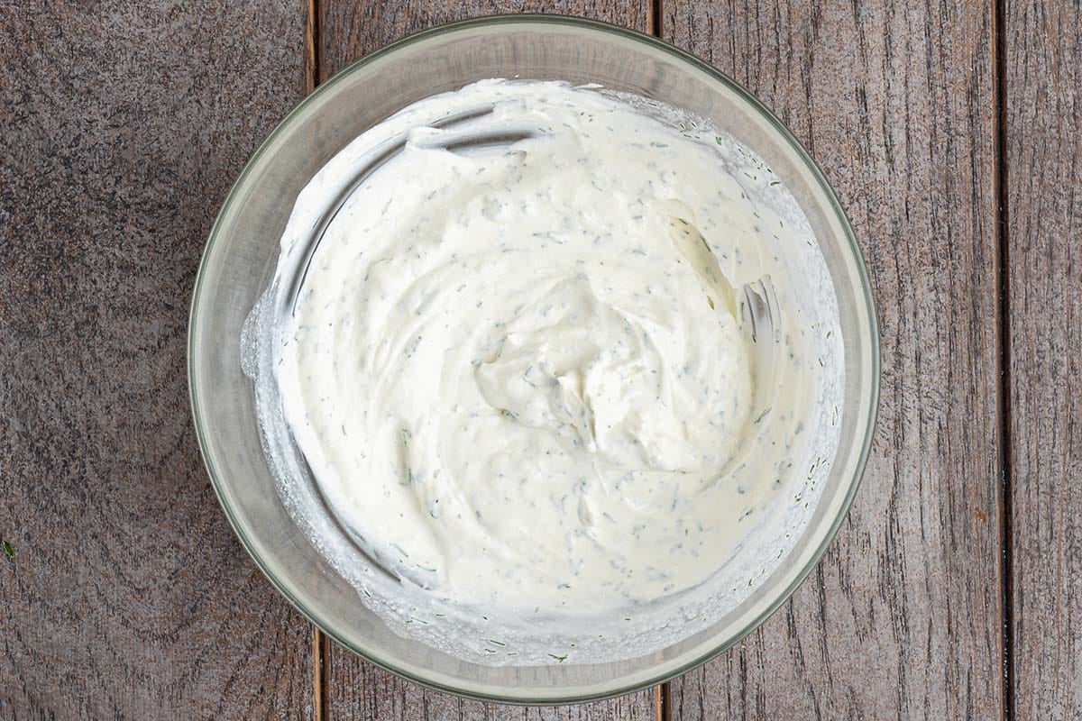 Creamy herb sauce in a glass bowl on a wooden surface.