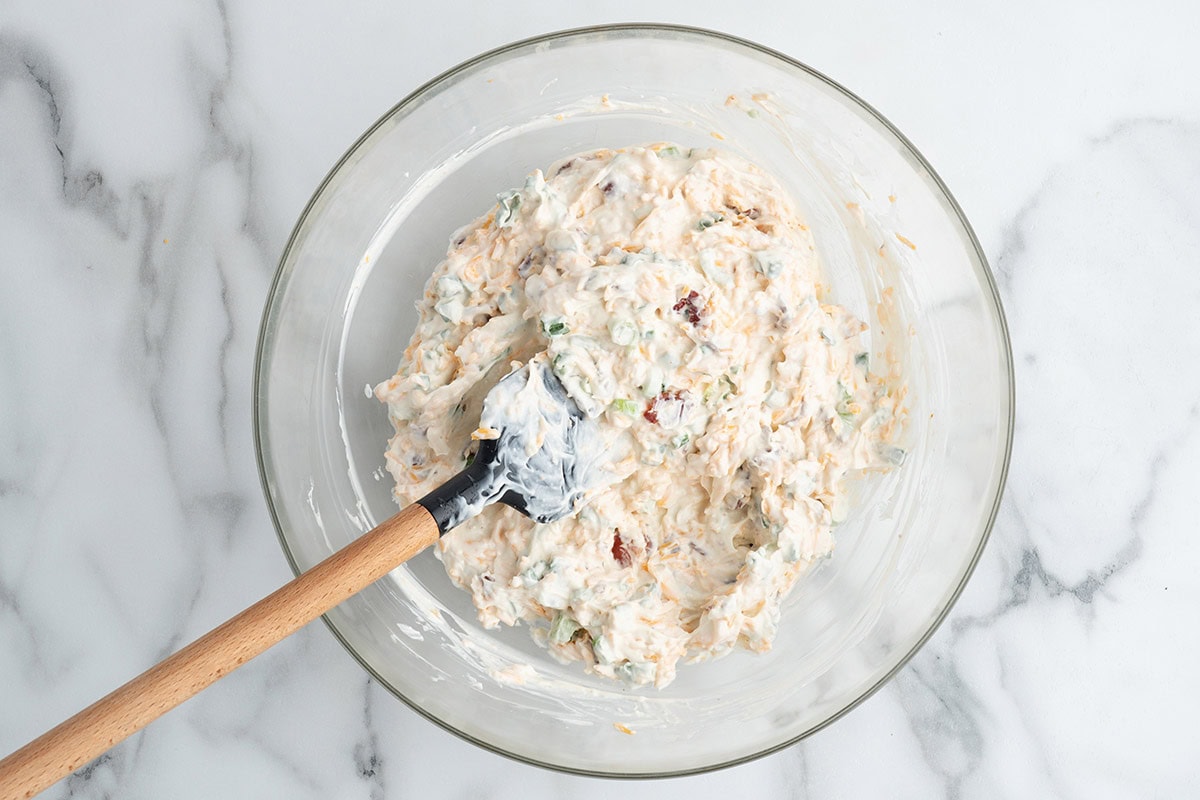 Fully mixed million dollar dip in a glass bowl with a rubber spatula.
