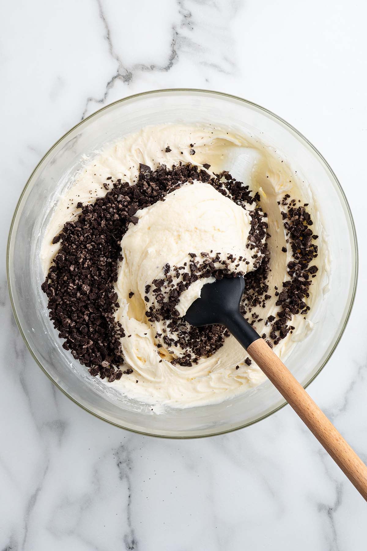 Oreo crumbs being folded into the white frosting with a spatula.