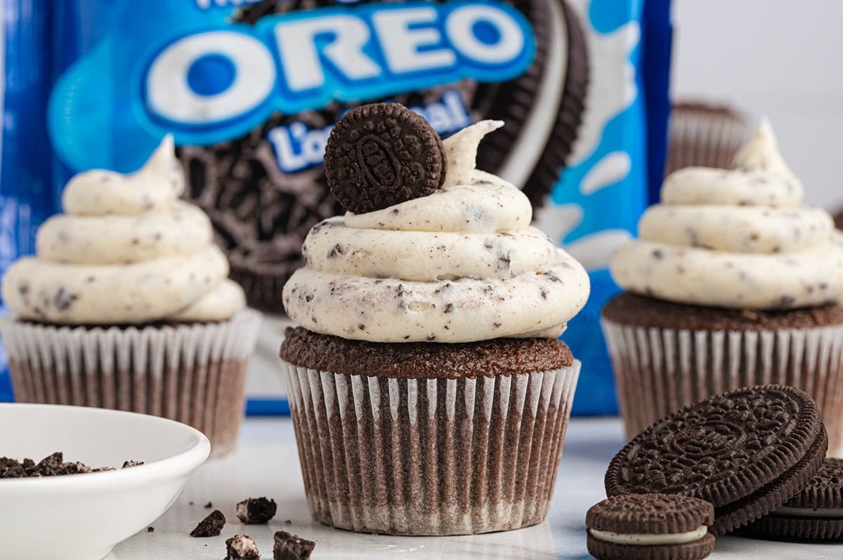 Chocolate cupcakes with cookies and cream frosting and Oreo cookies in the background.