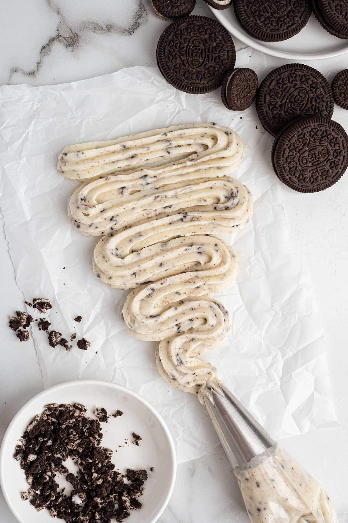 Cookies and cream frosting piped on parchment with crushed Oreos nearby.