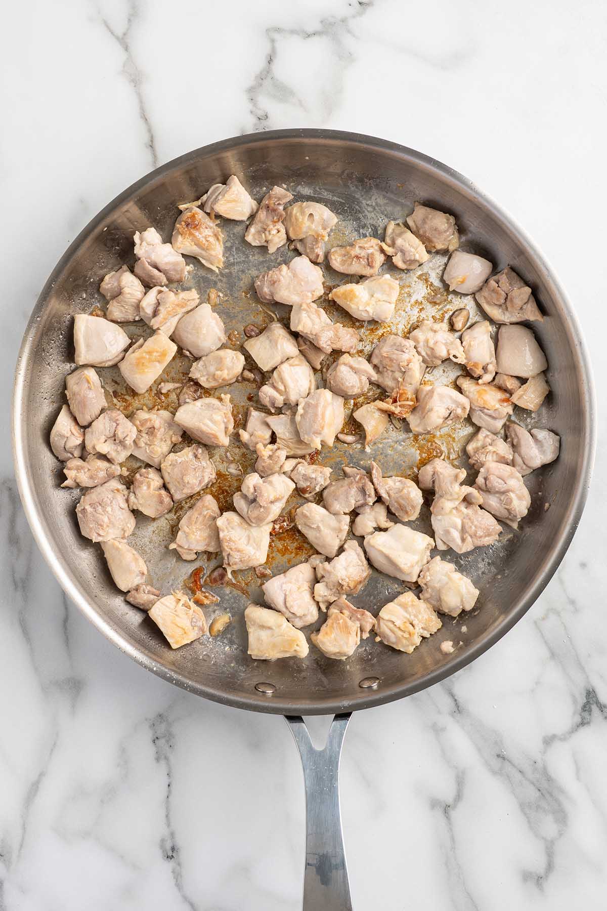 Diced chicken thighs cooking in a stainless steel skillet.