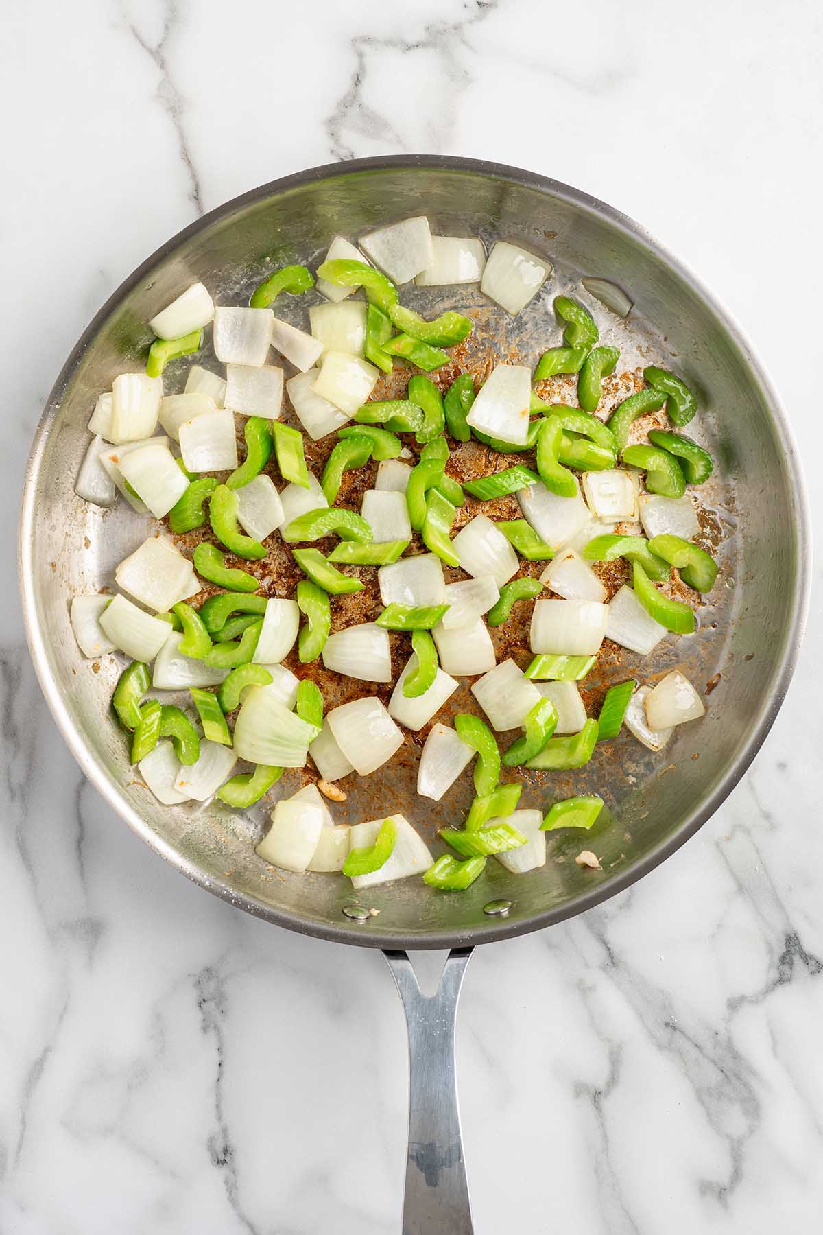 Chopped onions and sliced celery saut&eacute;ing in a stainless steel skillet.