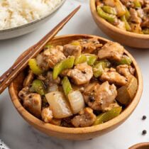 Panda Express pepper chicken in a wooden bowl with chopsticks, with celery, onions, and black pepper sauce, alongside a bowl of steamed white rice.
