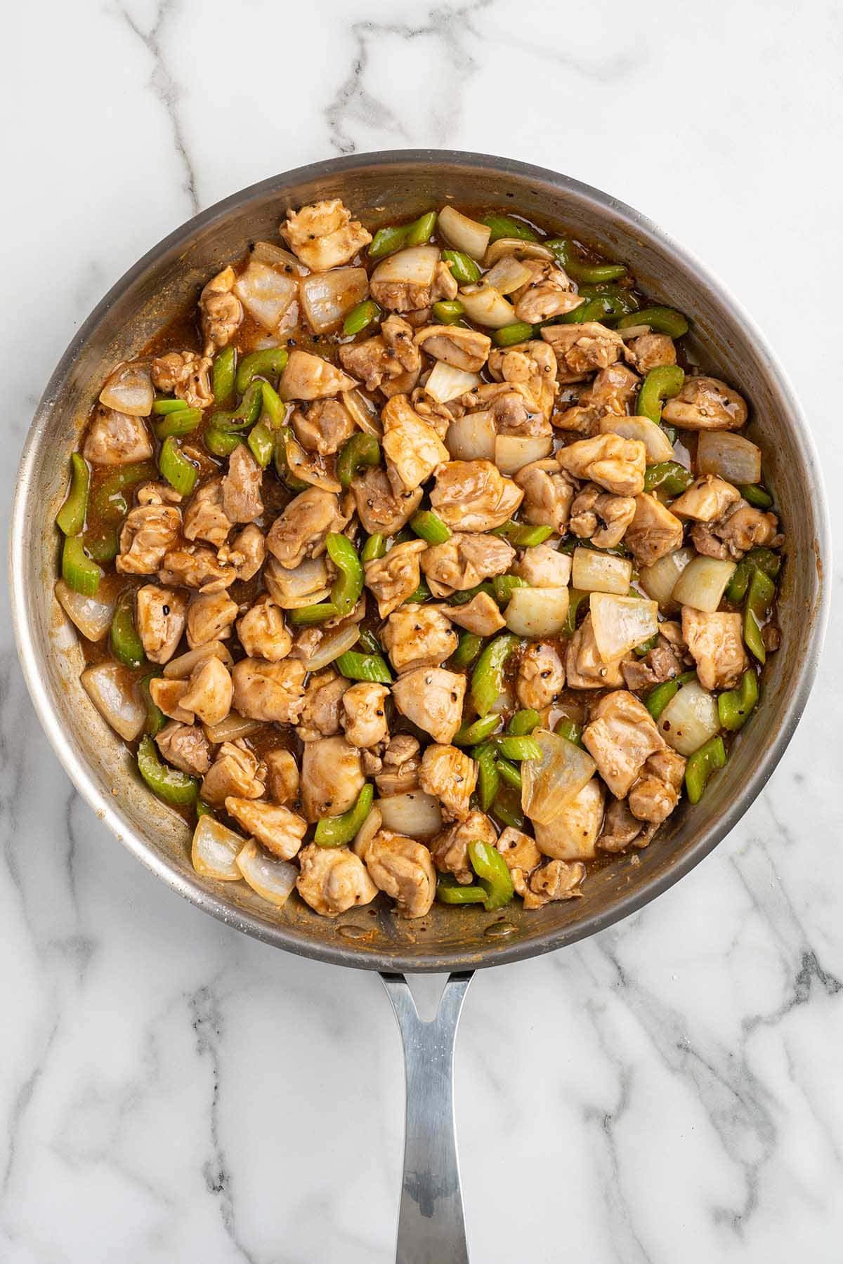 Finished pepper chicken stir-fry with celery, onions, and black pepper sauce in a skillet.