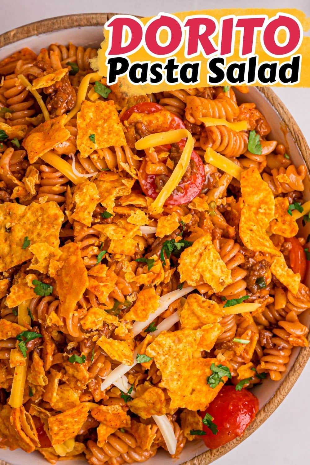 Close-up overhead view of Dorito pasta salad with rotini, Dorito chips, cherry tomatoes, and shredded cheese in a wooden bowl.