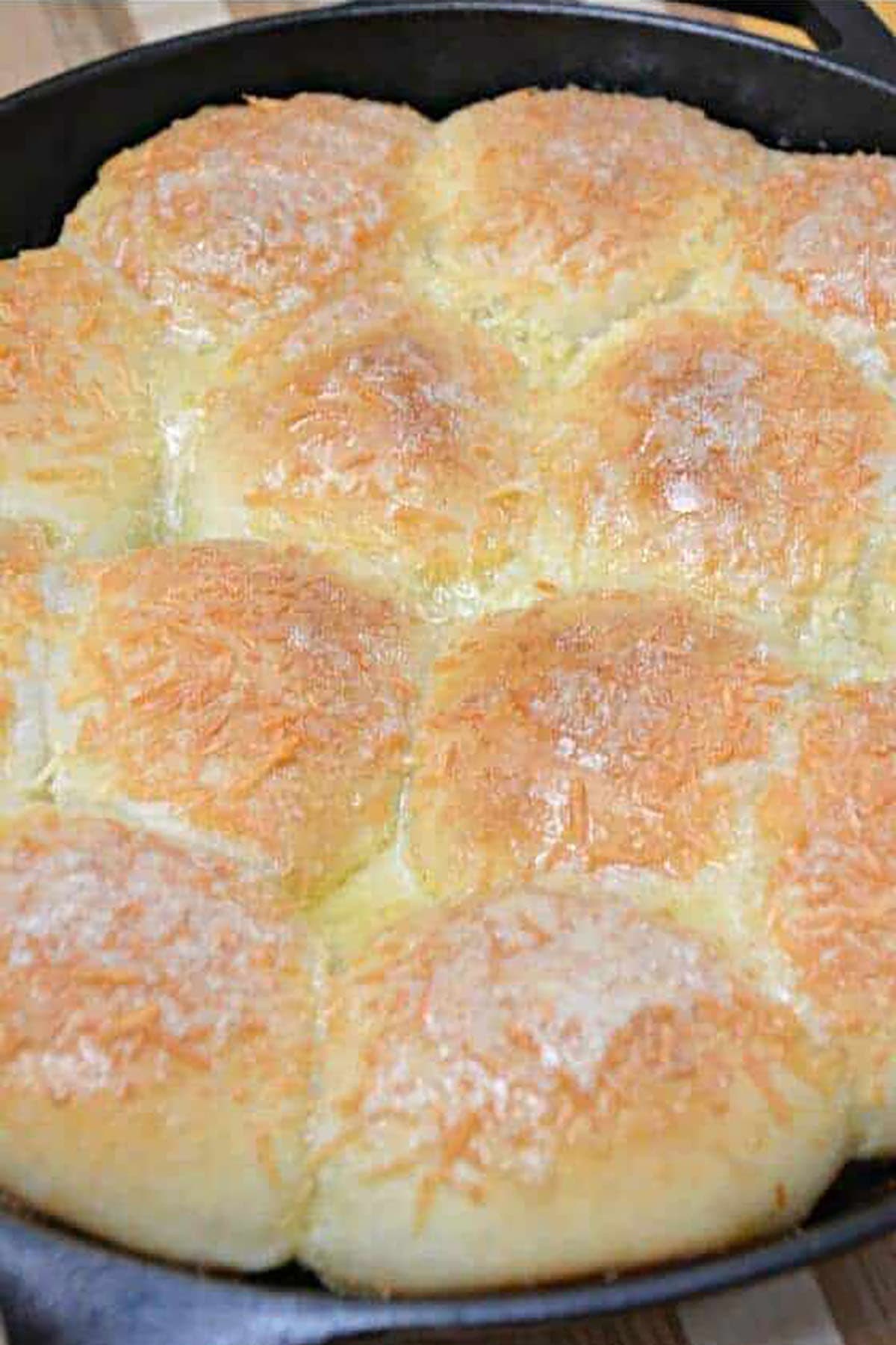 Close-up of fluffy golden mozzarella stuffed garlic rolls baked together in a cast iron skillet with a cheesy topping.