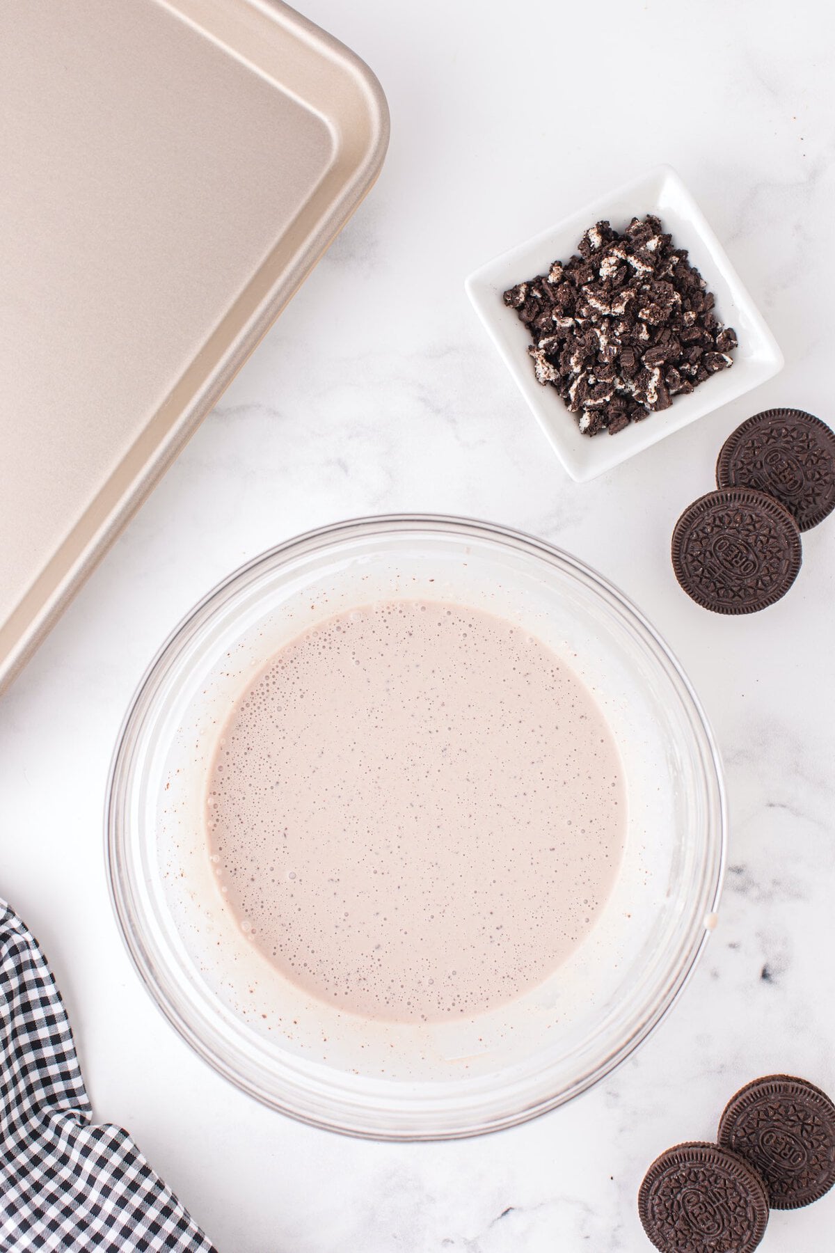 Oreo ice cream base mixture in a bowl with crushed cookies and a frozen pan ready for rolled ice cream prep.