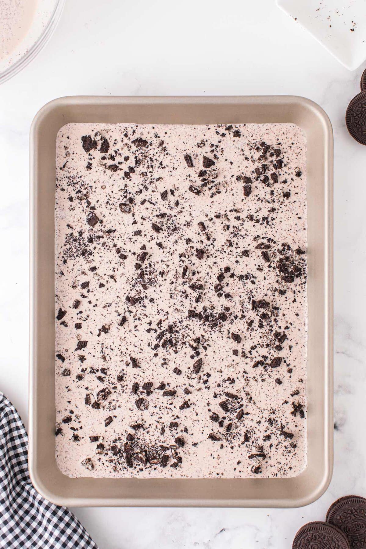 Oreo ice cream mixture spread in a chilled pan and topped with crushed cookies before freezing.